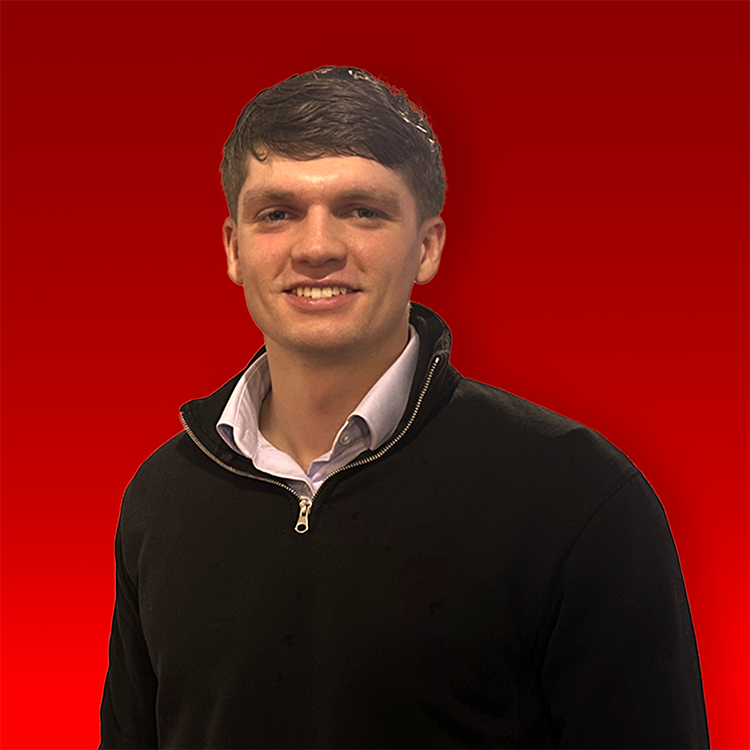 Milo Cook stood with black 3 1/4 zip on and light coloured shirt showing. Light brown hair and smiling 